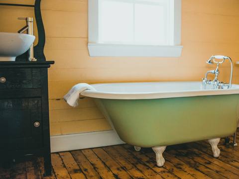 A painted green roll-top bath on a wooden floor