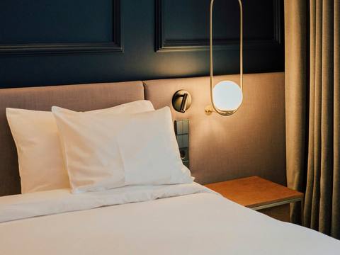 A bed with a brass wall lamp against a navy wall