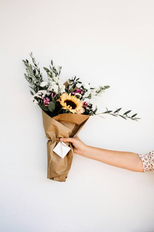 A hand holding a bouquet of sunflowers, eucalyptus and wild flowers wrapped in kraft paper