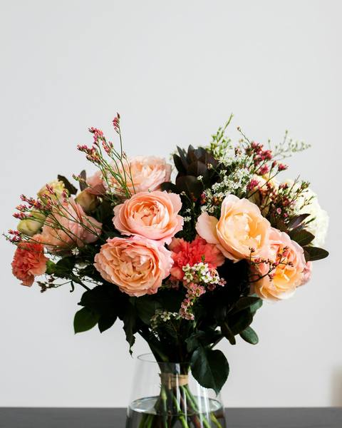 A hand-tied bouquet of peach garden roses and stocks in a glass vase
