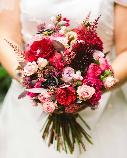 A bride in white holding a bouquet of red and pink roses