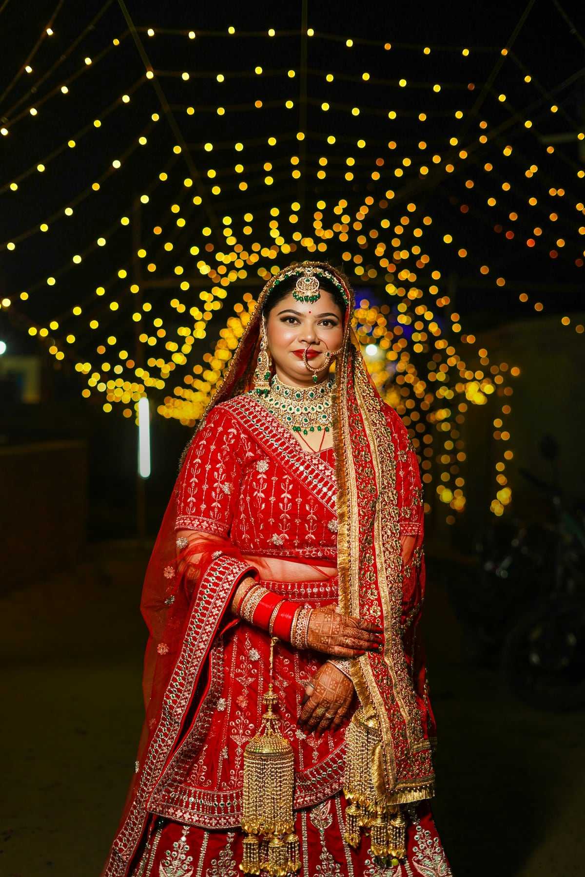 A bride in a red and gold lehenga under a canopy of lights