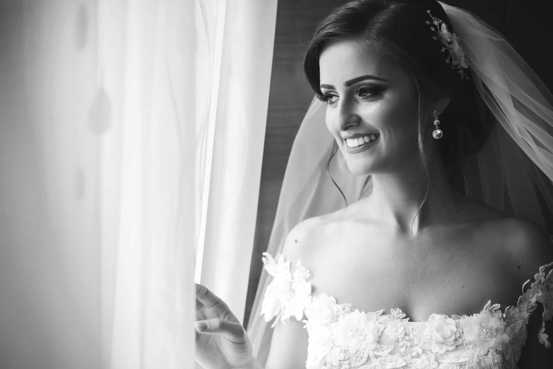 Black and white portrait of a bride smiling by a window