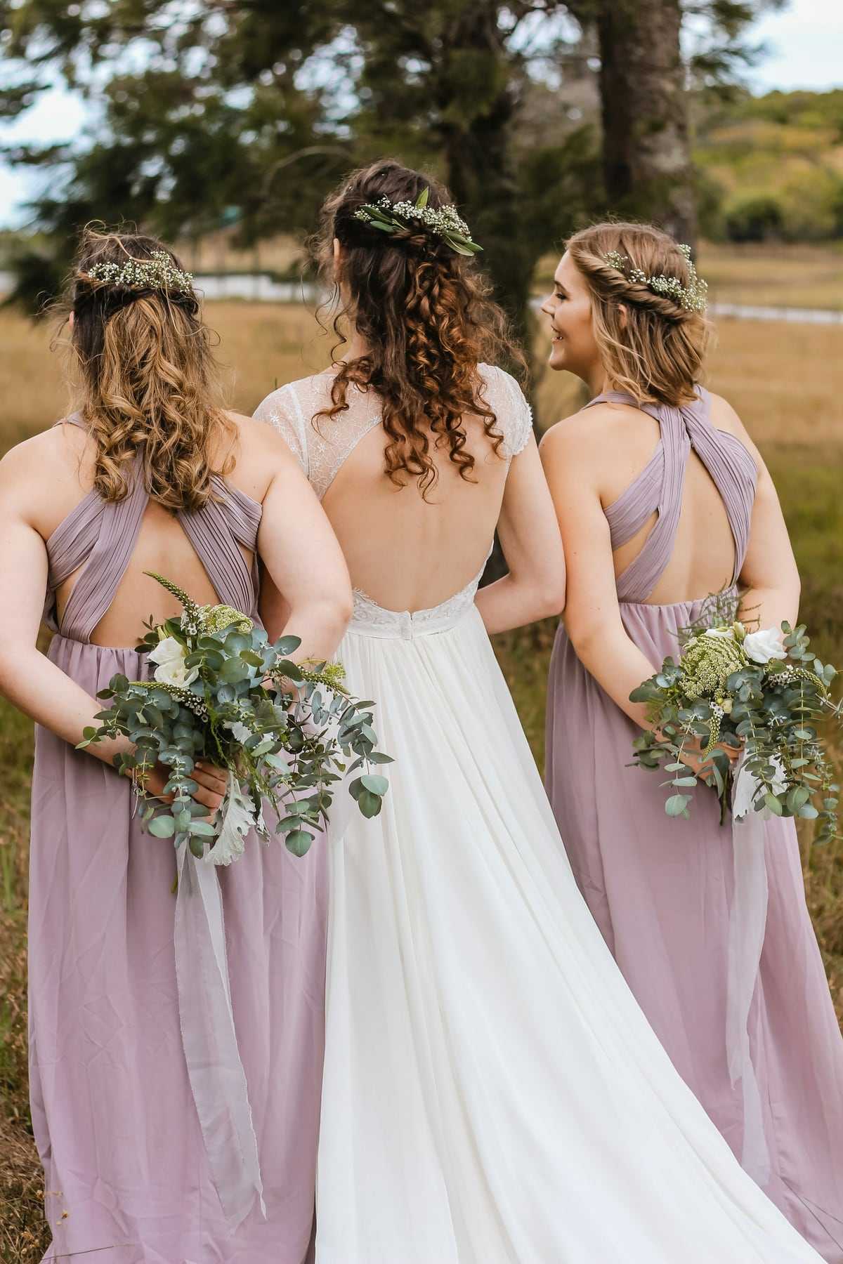 Bridesmaids in lilac dresses walking beside the bride, seen from behind