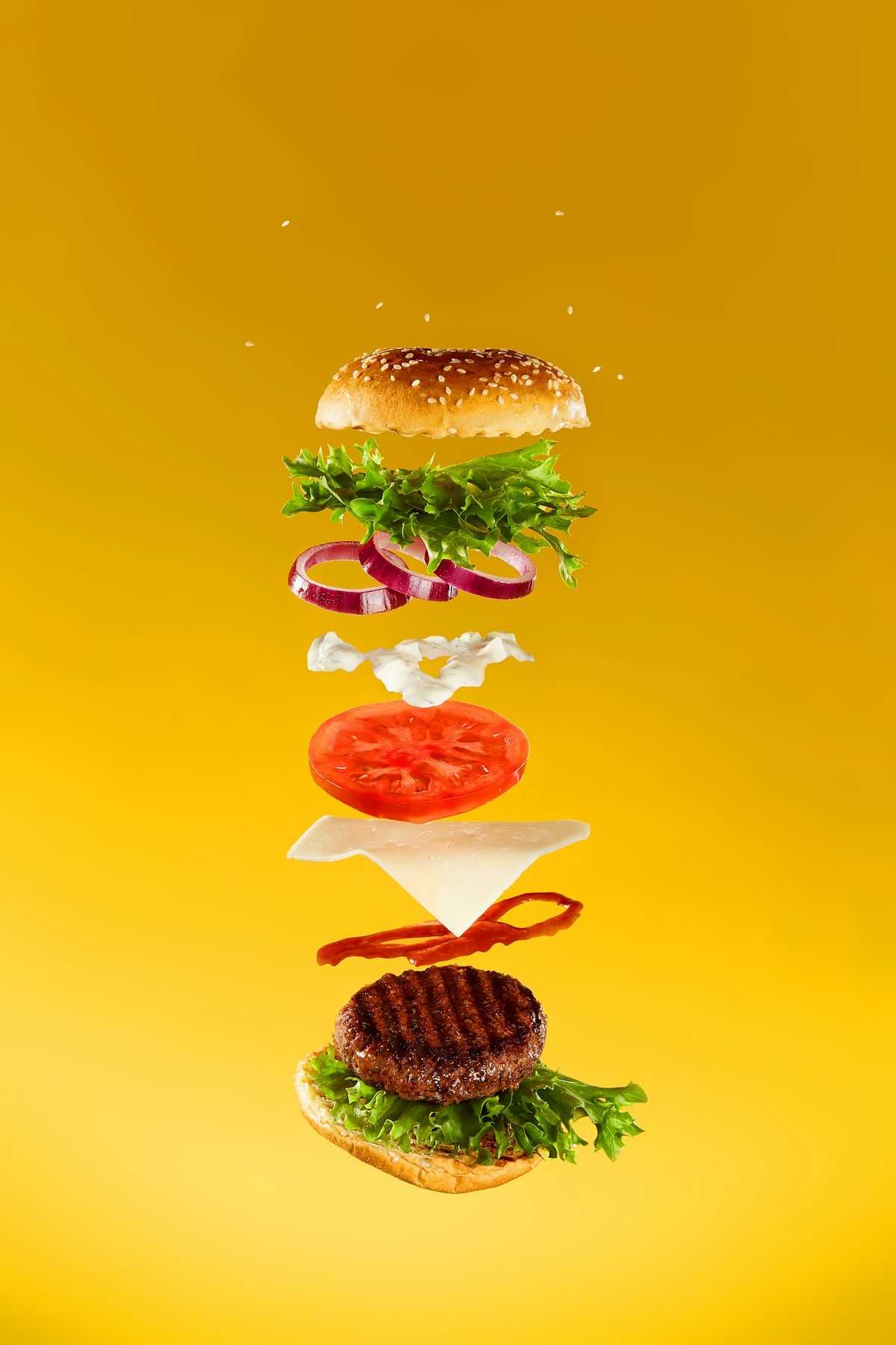 A burger floating apart into bun, patty, cheese, tomato and lettuce