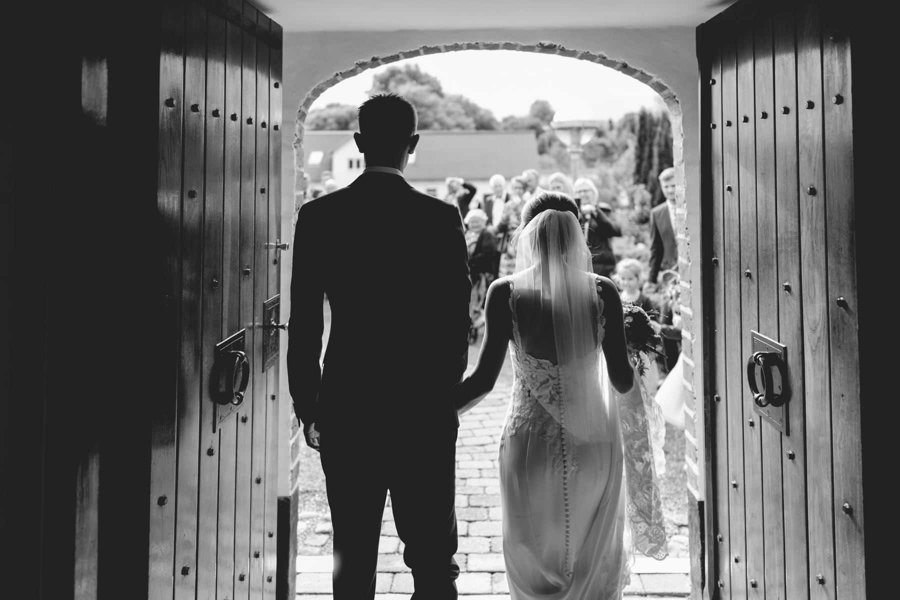 Black and white photo of a groom silhouetted in a church doorway