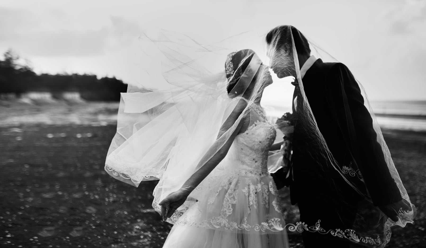 Black and white photo of a couple embracing as the veil lifts in the wind