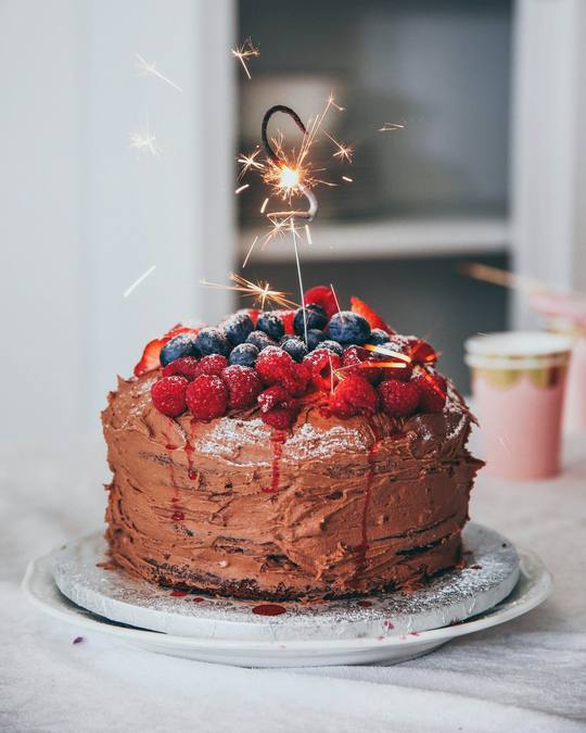 A chocolate celebration cake topped with fresh berries and a sparkler