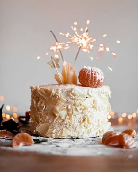 A semi-naked cake with a sparkler and fruit on top