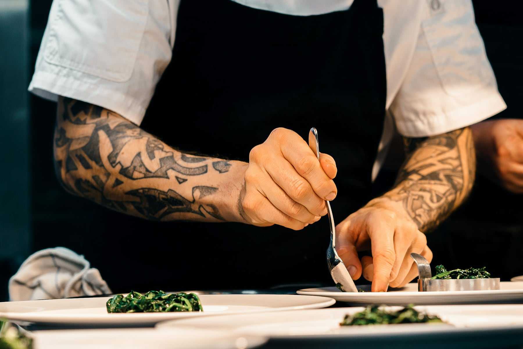 A chef placing herbs on a plate with tweezers