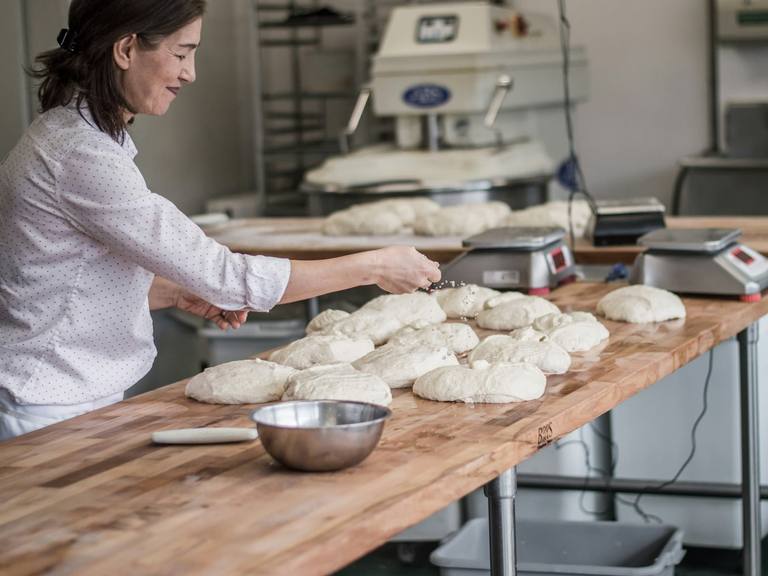 A baking class shaping dough at a long wooden table