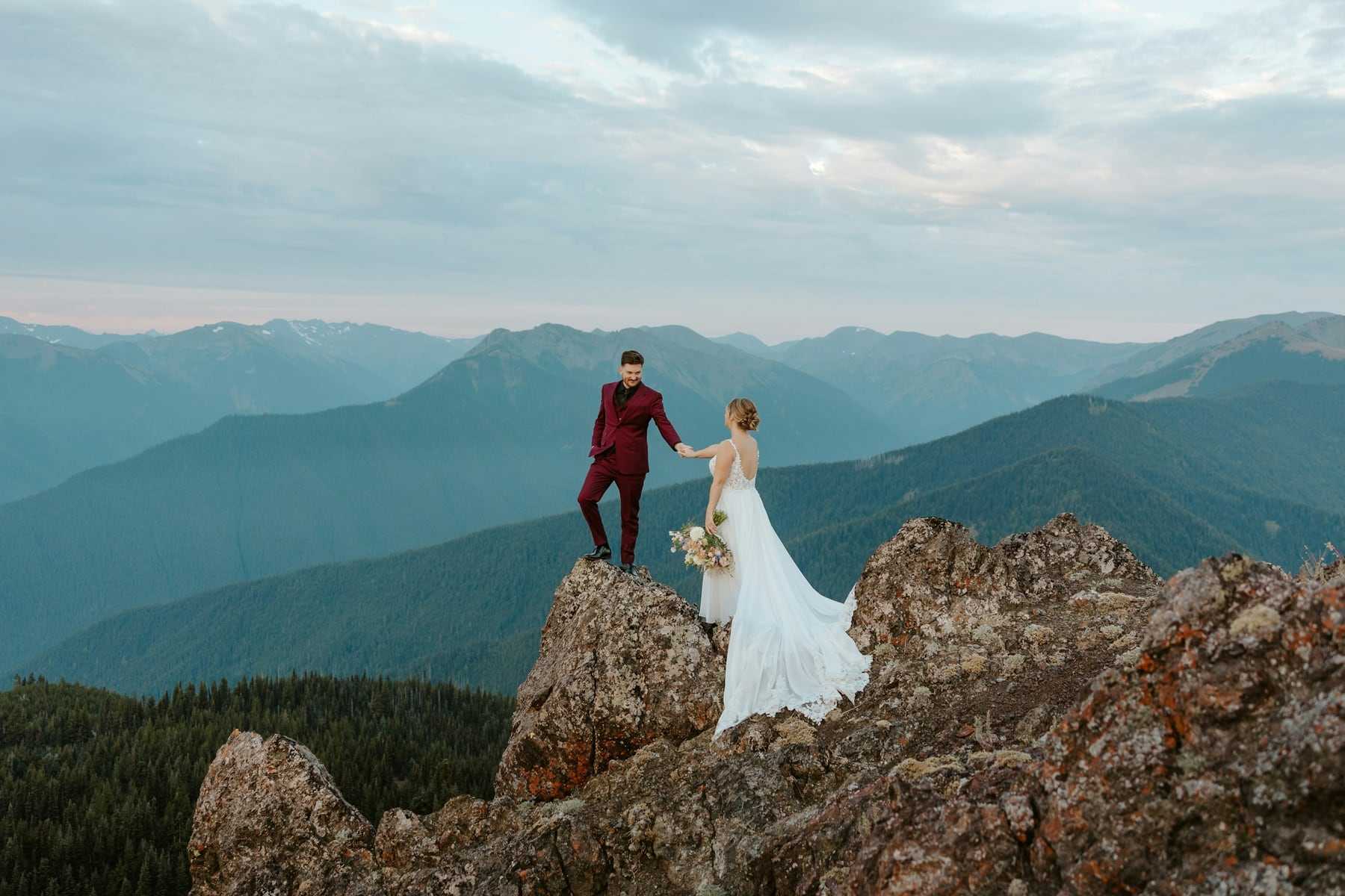 A bride and groom standing on a rocky outcrop above a wide valley