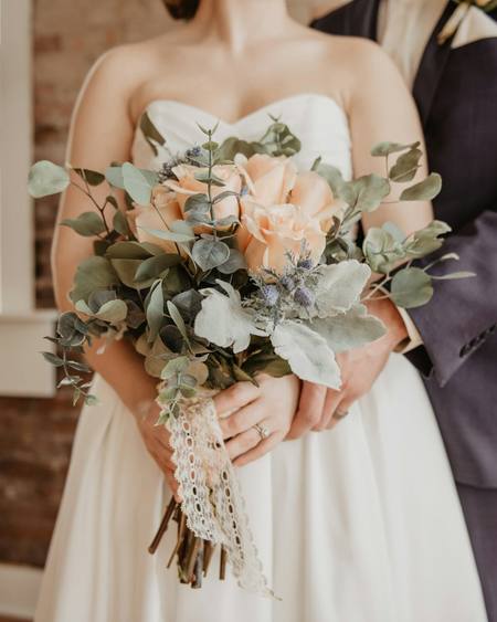 A couple holding a soft peach and green bridal bouquet