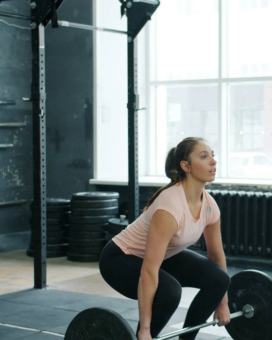 A coach watching a client set up for a deadlift in a bright gym