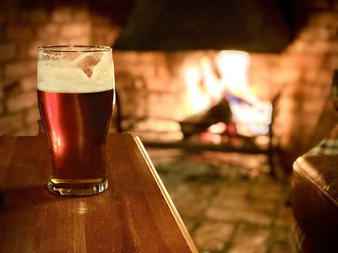 A pint of dark ale on a table by the fire
