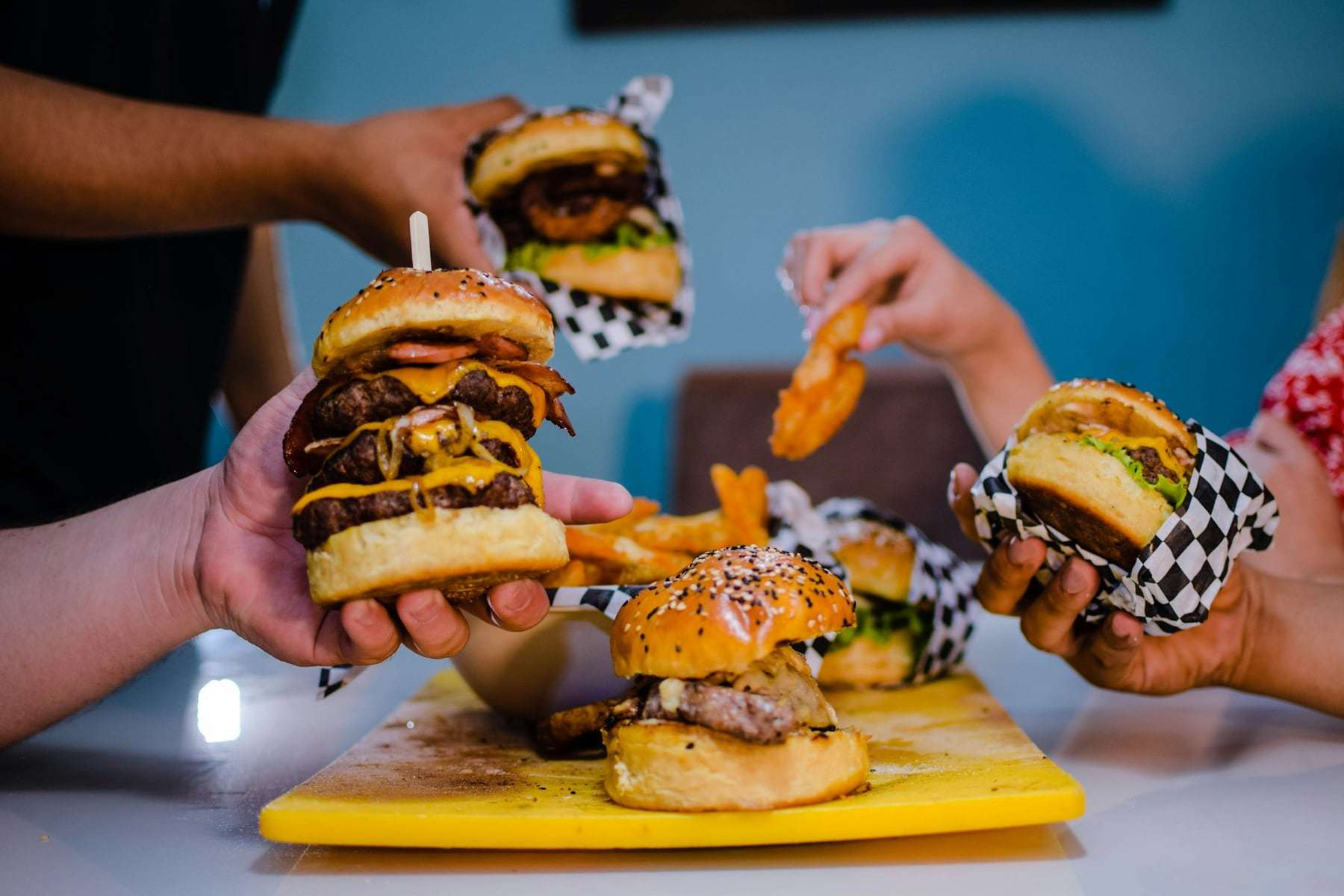 Friends reaching for stacked burgers on a yellow tray
