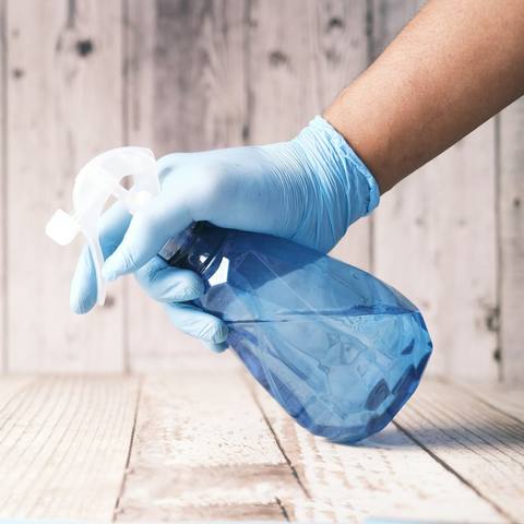 A gloved hand wiping a counter with a spray bottle
