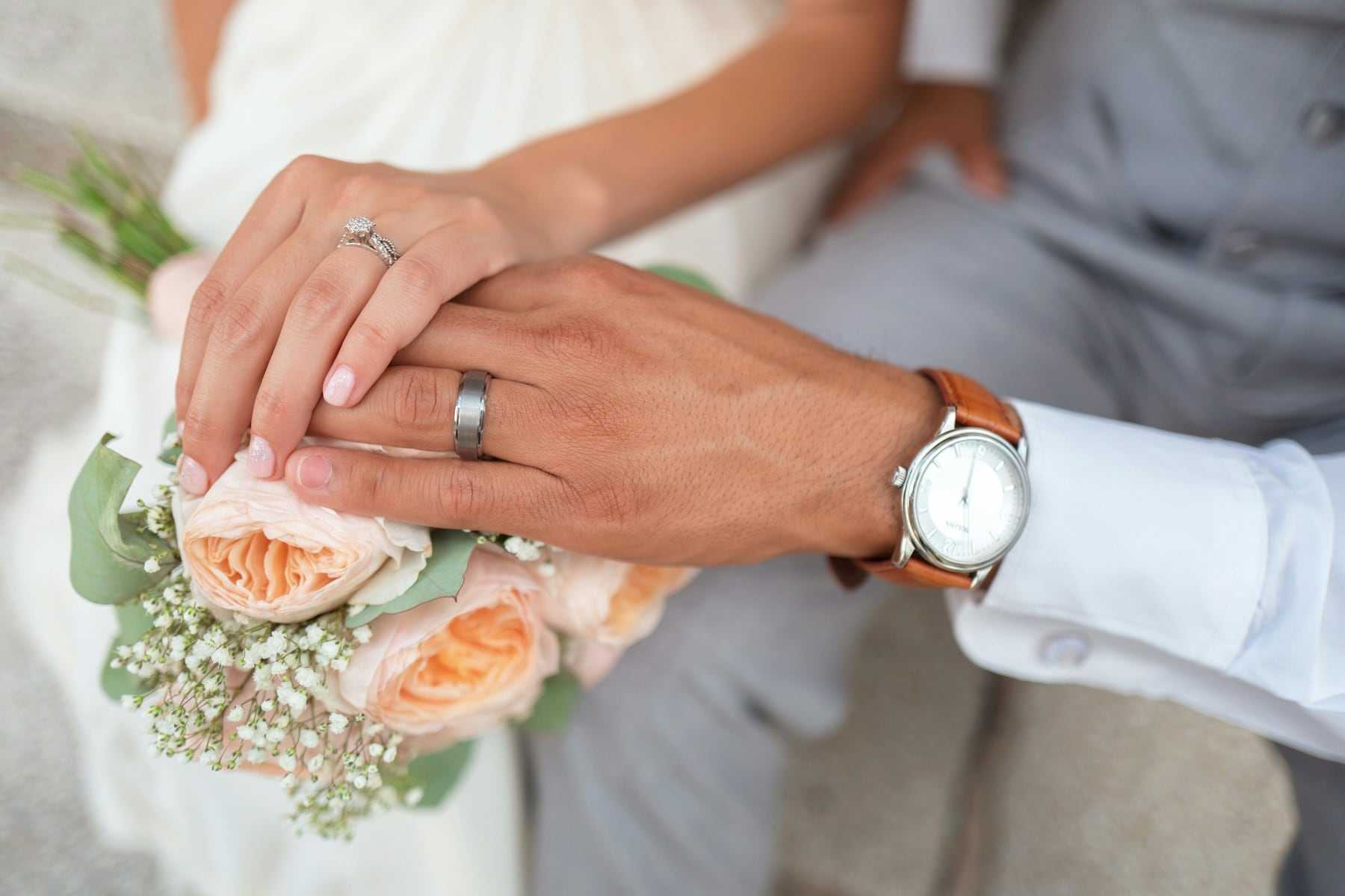 A couple’s hands with wedding rings resting on a bouquet
