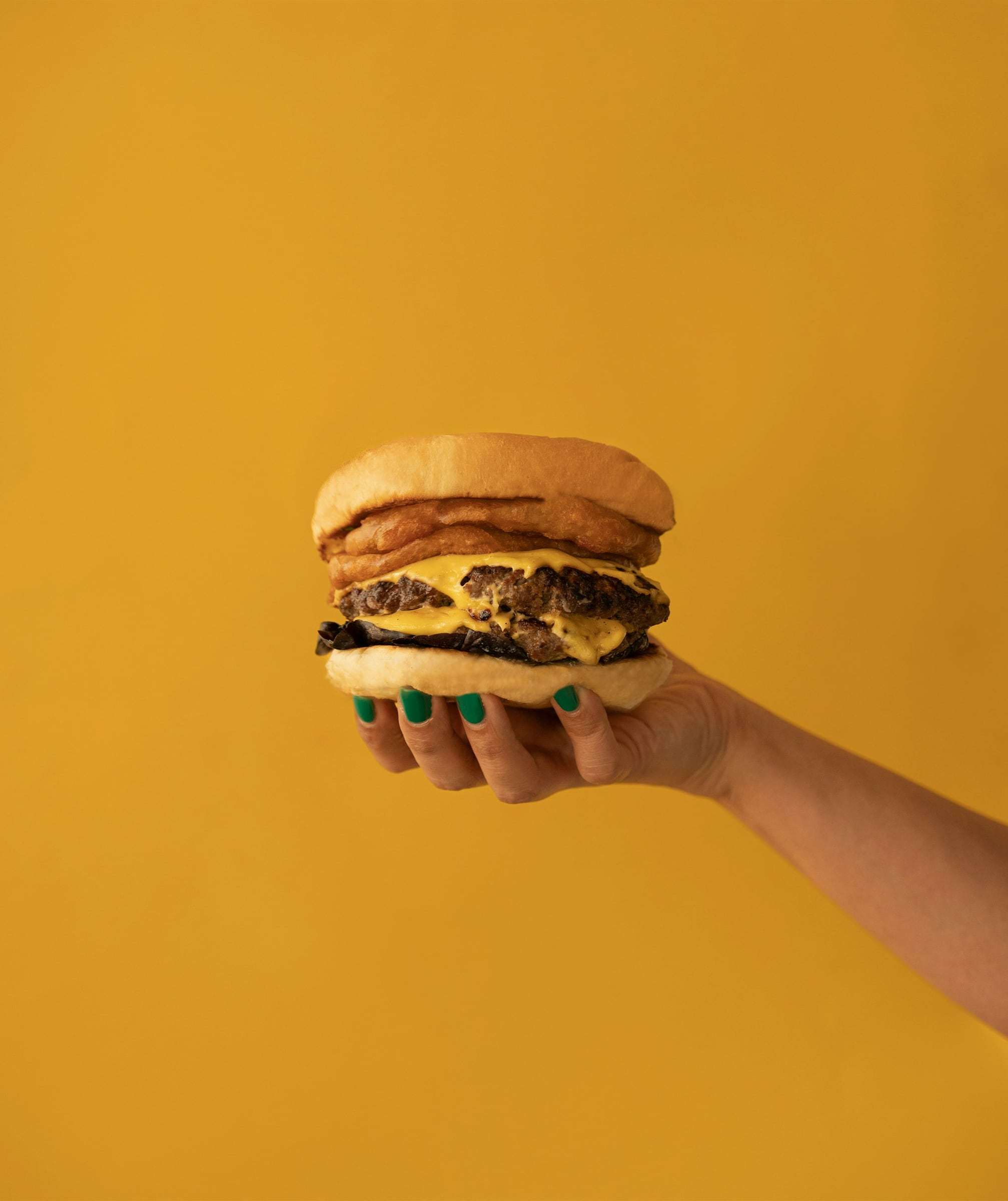 A hand holding up a double cheeseburger against a yellow wall