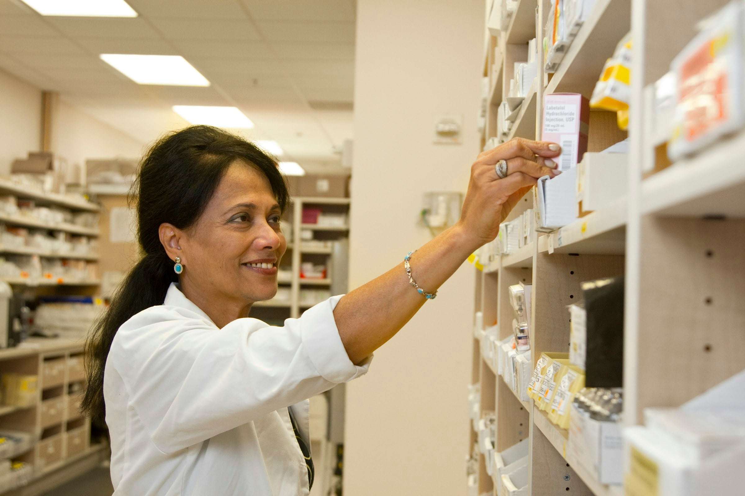 A smiling pharmacist reaching for medicine on the shelves
