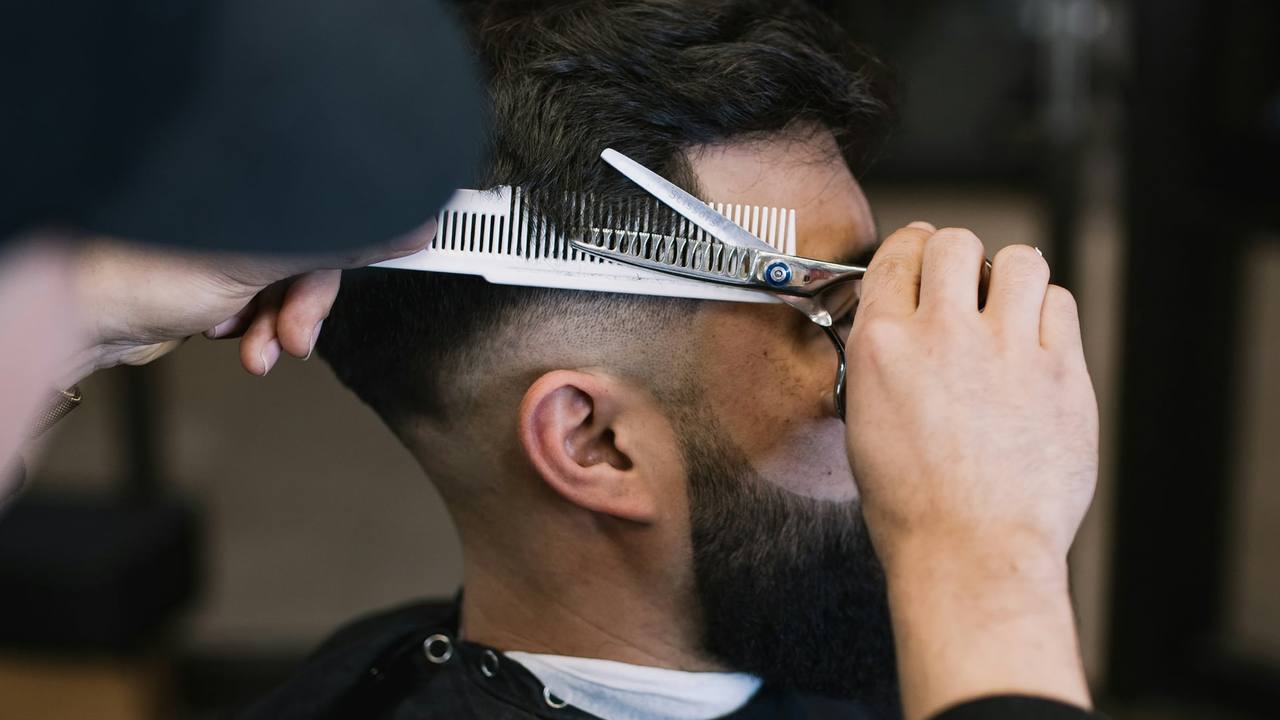 A barber cutting a client's hair with scissors and a comb