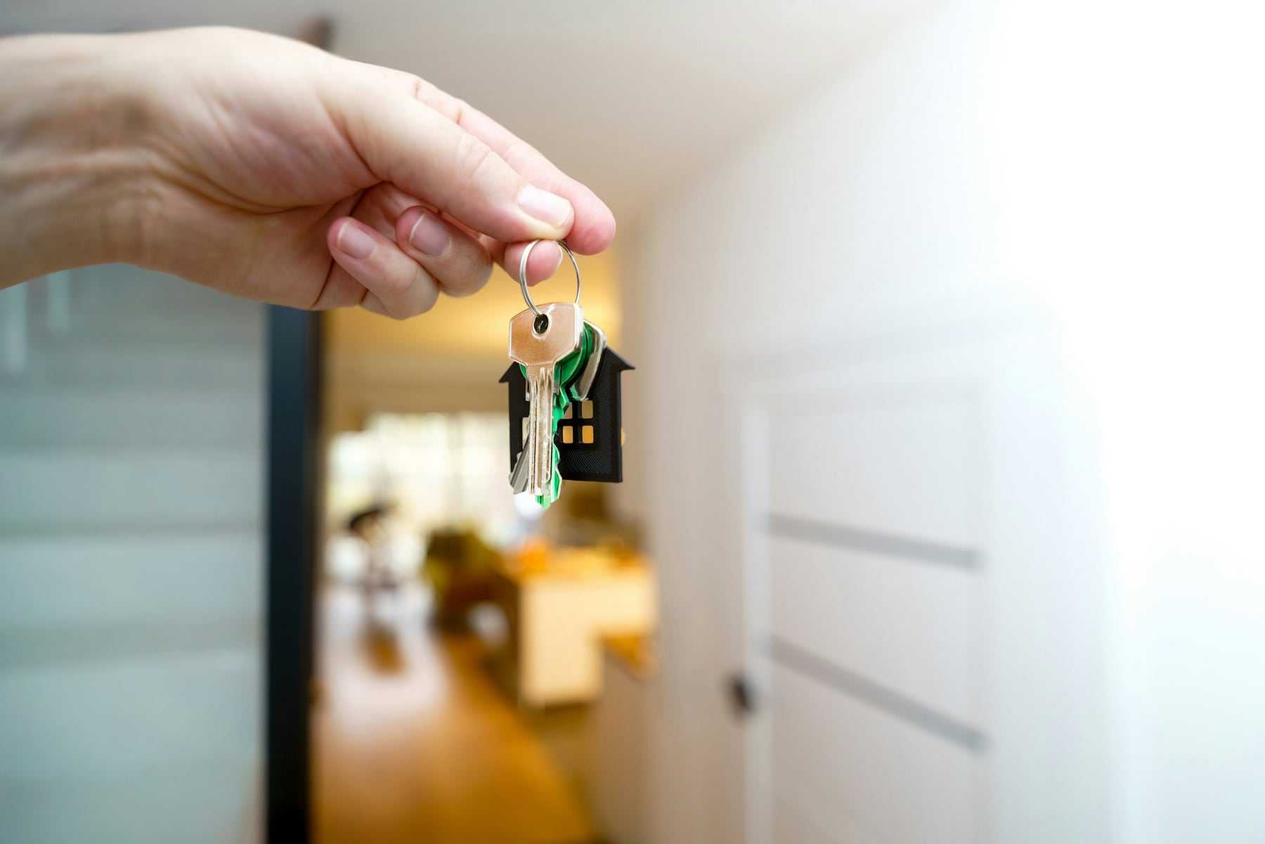 A hand holding out a set of house keys in a hallway