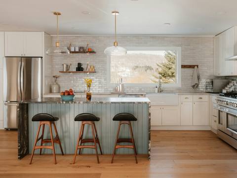 A white kitchen with a sage-green island and bar stools