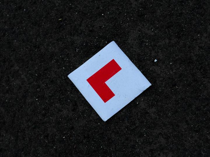 A red L-plate lying on dark tarmac