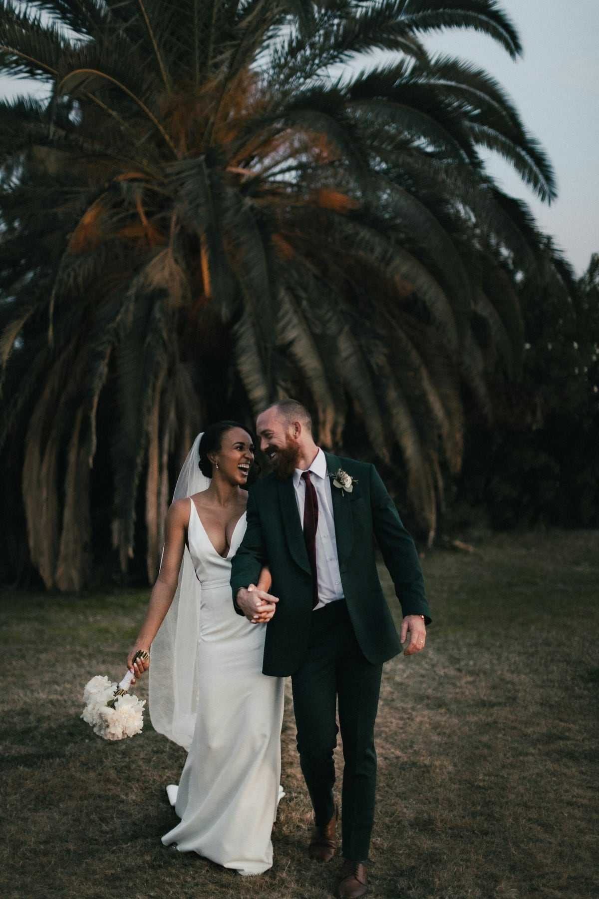 A couple laughing as they walk under tall trees