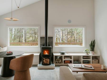 A white living room with a black wood stove and two big windows