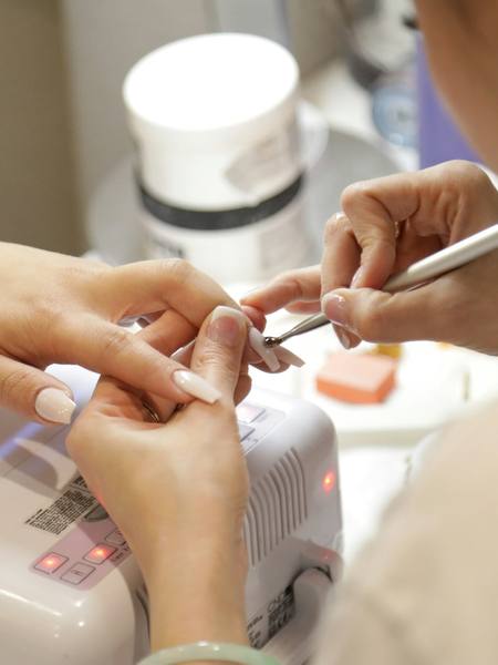 A manicurist painting a client’s nails at a salon desk