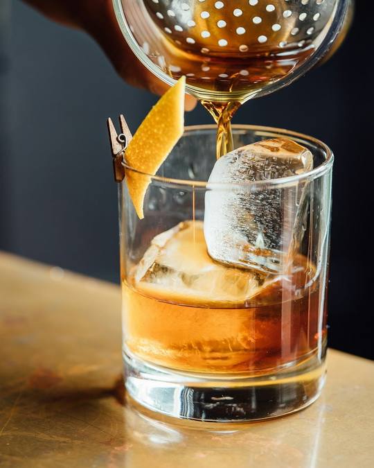 An amber whisky cocktail being poured over ice