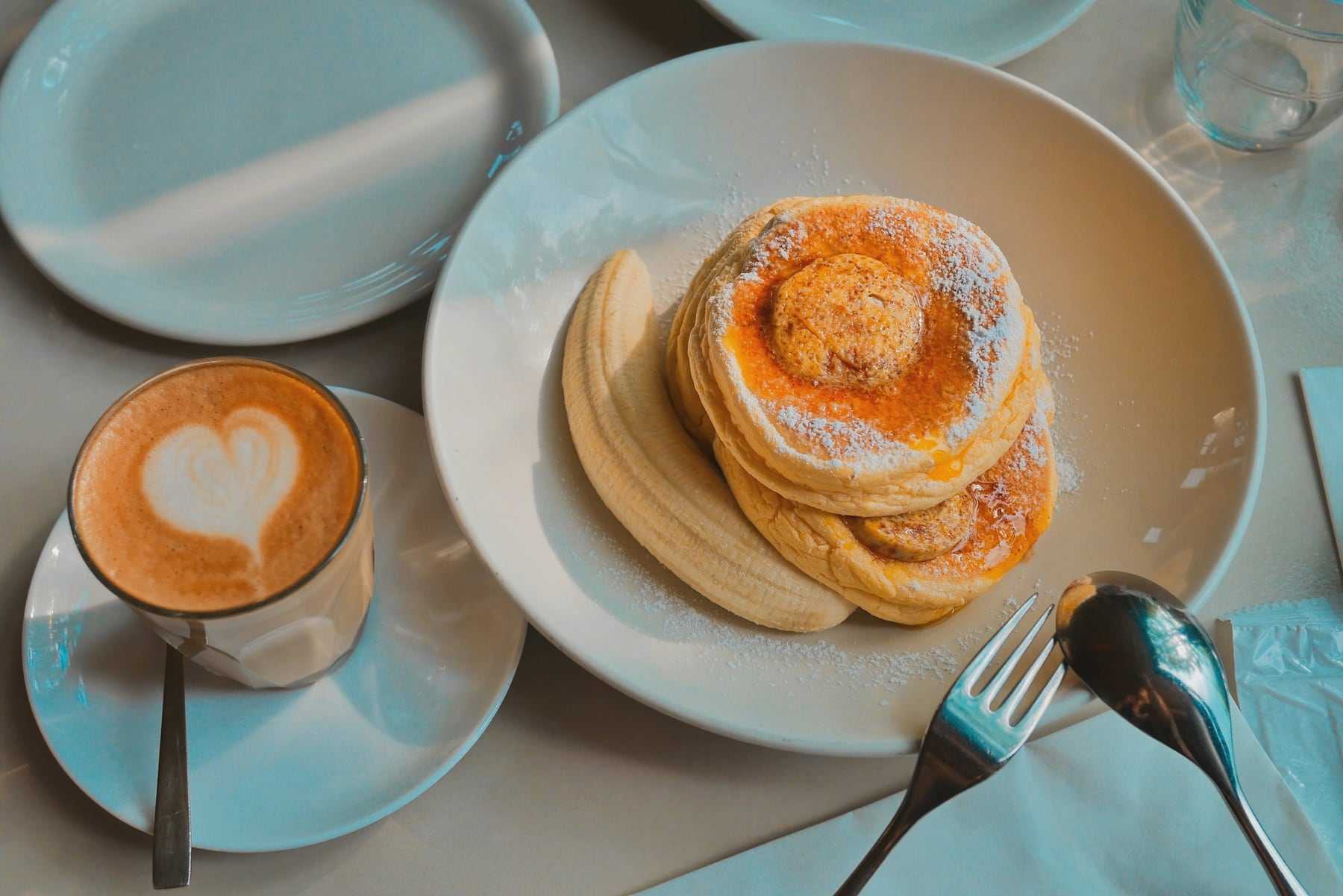 A stack of pancakes next to a latte with a heart