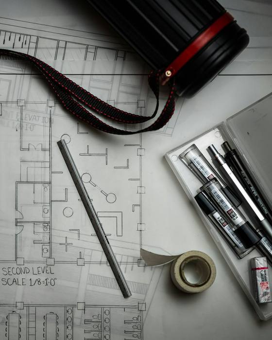Architectural drawings on a desk with pens and a tape measure