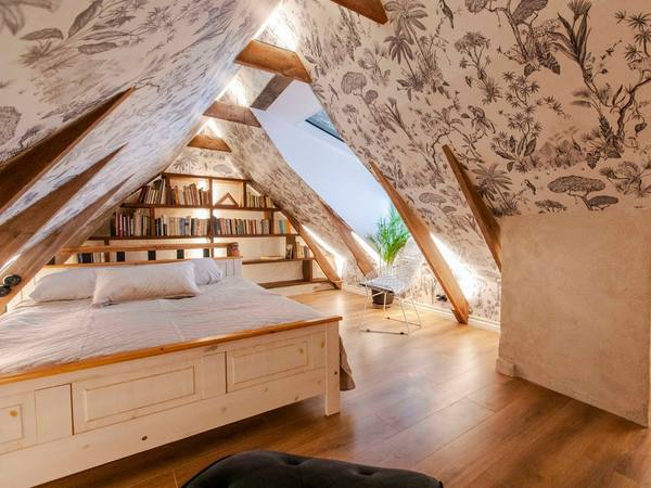 An attic bedroom with patterned wallpaper and bookshelves under the eaves