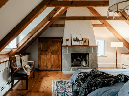 A beamed bedroom with a stone fireplace and an armchair