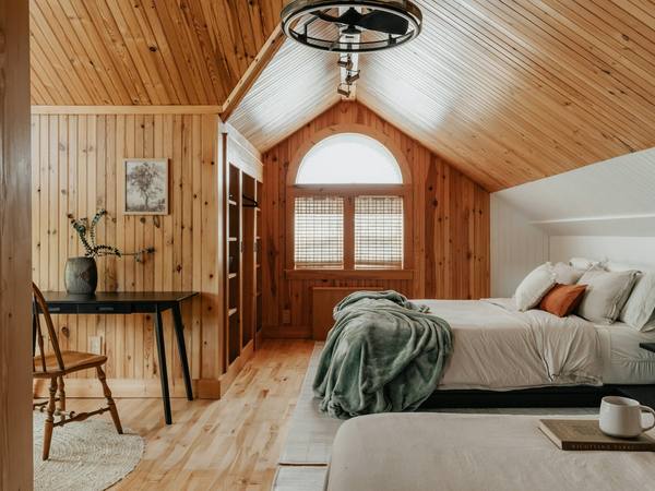 A wood-panelled bedroom with an arched window and a reading chair
