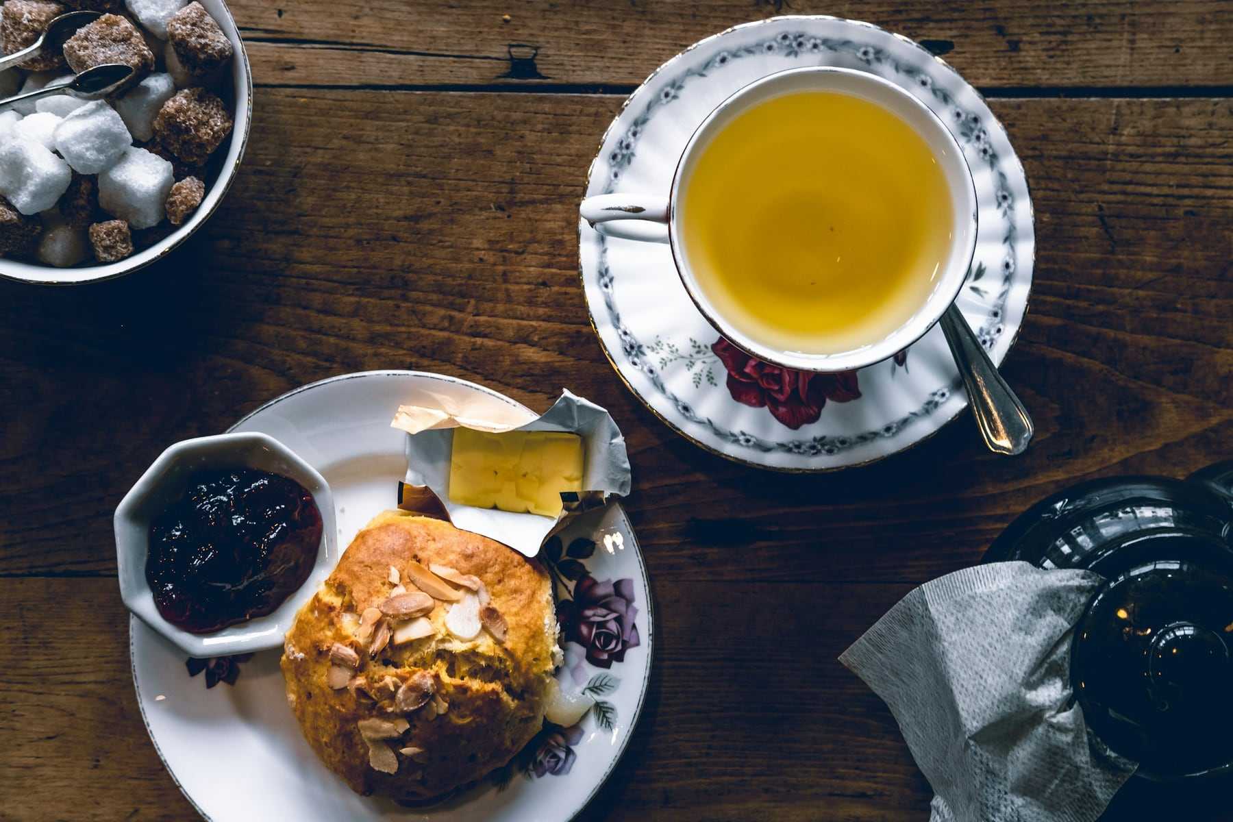 A scone with jam next to a cup of tea
