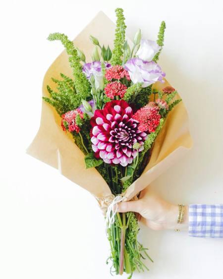 A loose bouquet of dahlias and grasses in kraft paper
