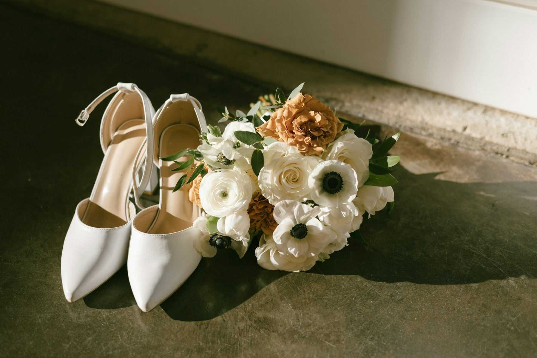 White bridal shoes beside a small bouquet of white flowers