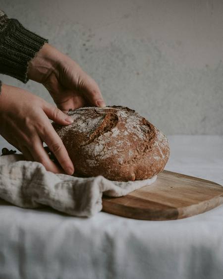 A baker lifting a crusty sourdough loaf