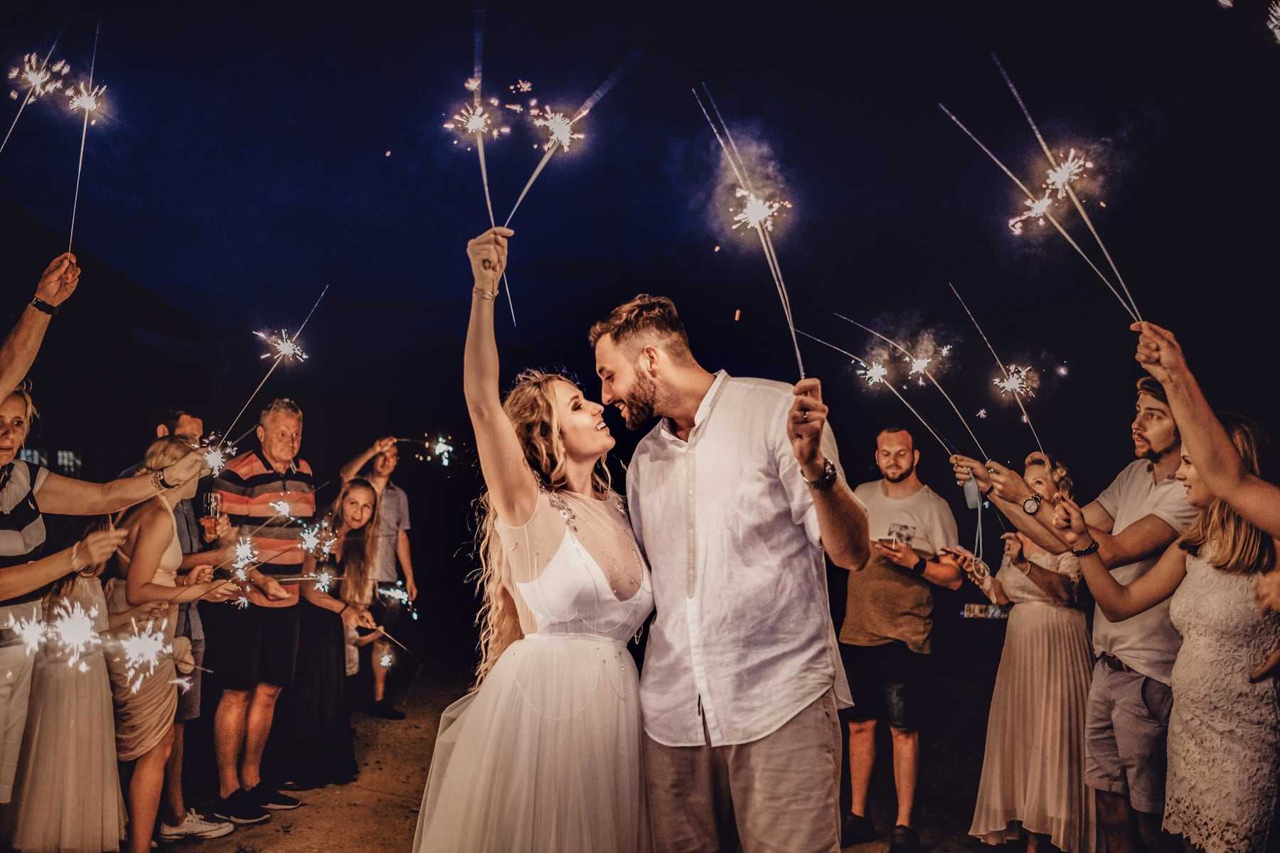 The couple kissing as guests hold sparklers above them at night