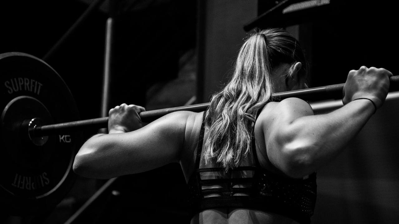 A woman holding a barbell across her shoulders in a dark gym