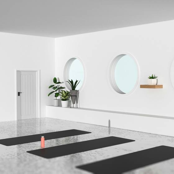 A bright, empty yoga studio with round windows and mats laid out