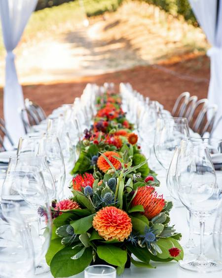 A long table runner of orange and red flowers between glasses