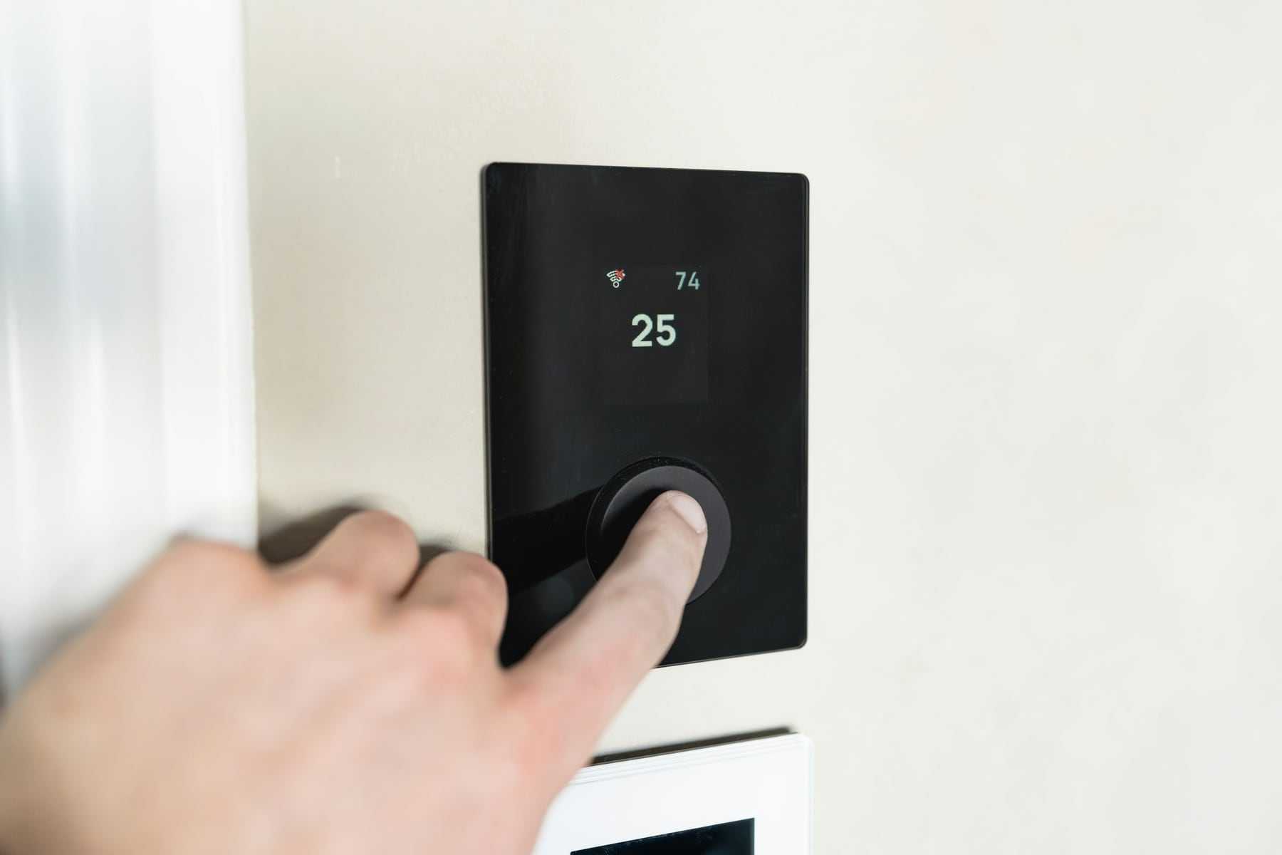 A hand adjusting a smart thermostat on a white wall