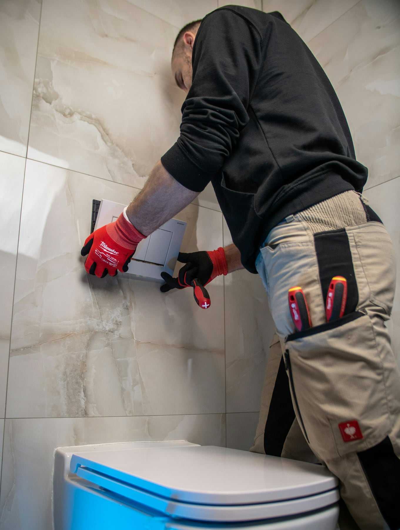 An engineer in work trousers and red gloves fitting a new toilet
