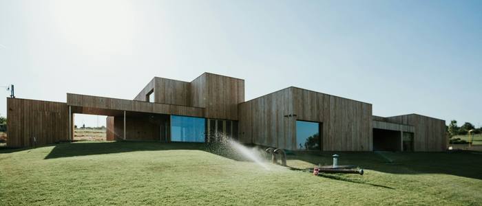 A long, low timber clad house on a lawn in the countryside