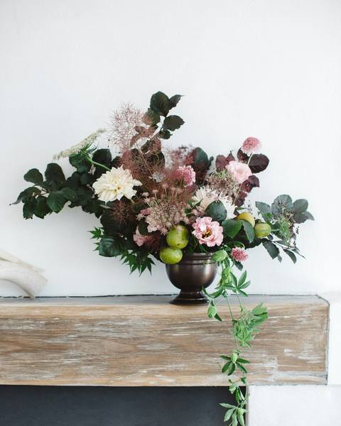 An arrangement of dark roses and foliage in an urn on a mantelpiece