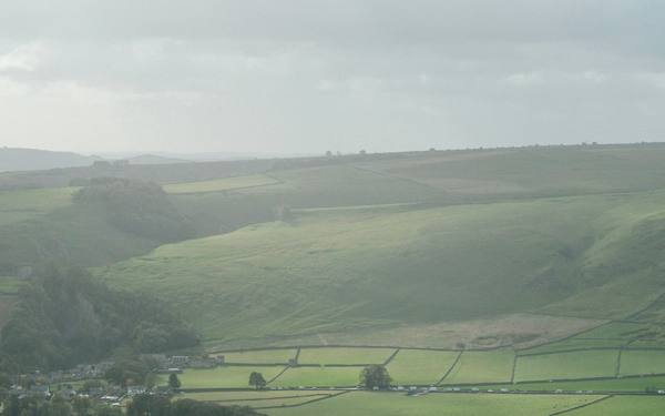 Green fields and drystone walls in the valley below a hill